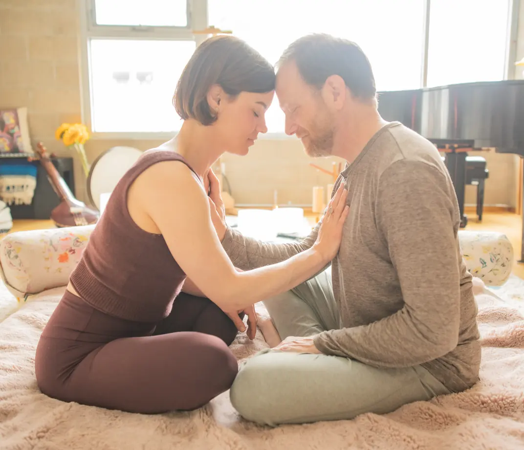 A couple sitting close with foreheads touching, her hand resting on his heart, in the sunlit Word of Mouth studio in Los Angeles