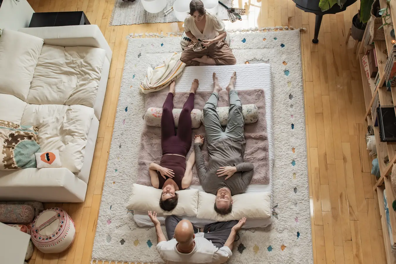 A couple lying side by side on a mat, resting, with a practitioner seated at their heads and another at their feet, seen from above in the Word of Mouth studio