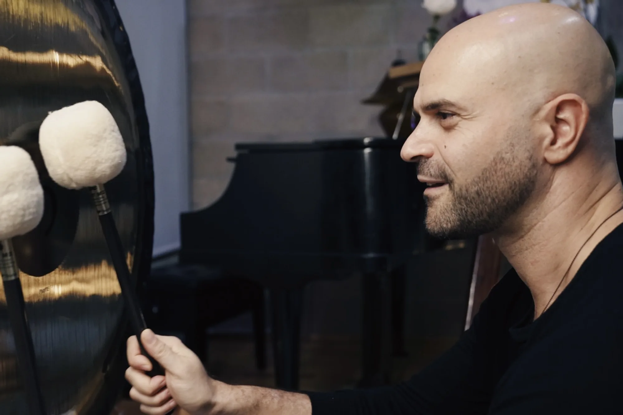 Yonatan in profile holding two felt mallets to a large gong in the Word of Mouth studio