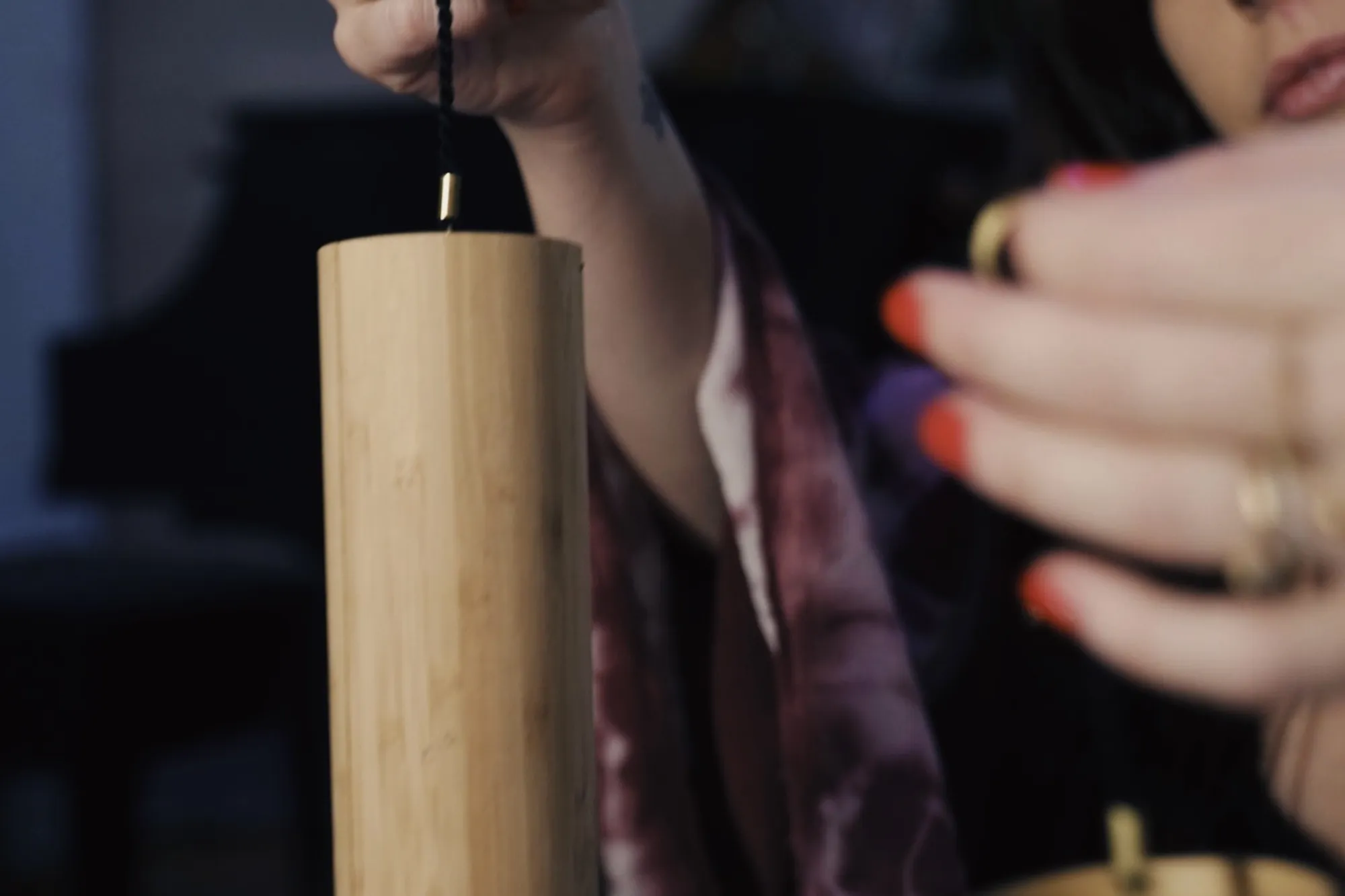 A hand with red nails and gold rings lifting a bamboo chime in a dark room at Word of Mouth