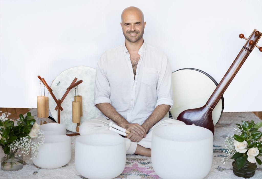 Yonatan Elkayam seated cross-legged with crystal bowls and tanpura