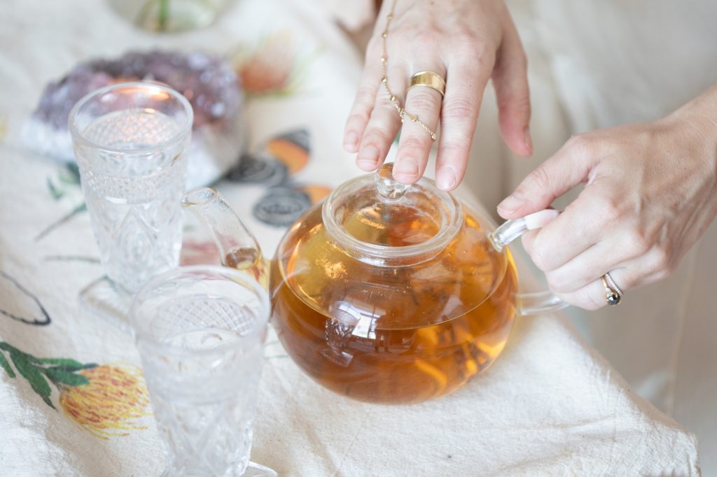 Hands resting on a glass teapot beside an amethyst candle