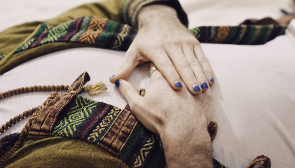 Healing hands with mala beads resting gently on a client's chest during a Reiki session