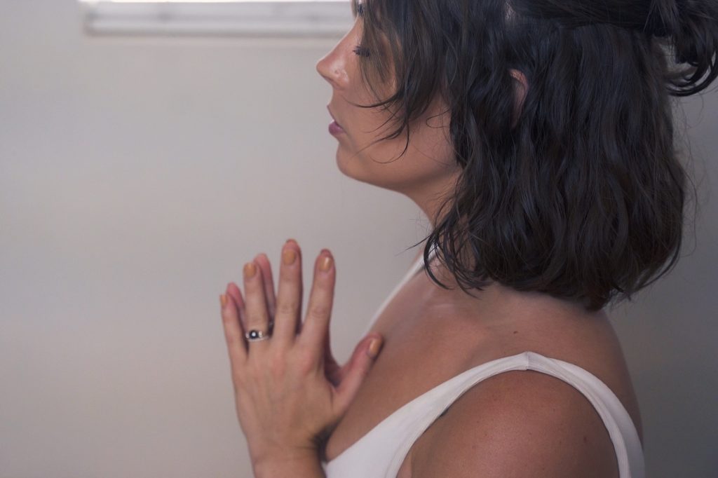A woman in profile with her hands pressed together at her own heart, the way a Reiki self practice opens.